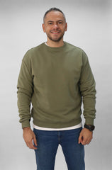 Man wearing an olive green sweatshirt and blue jeans against a plain background
